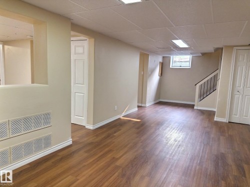 Finished lower level featuring wood-finish flooring, neutral paint, a drop ceiling with integrated lighting, a window, and a white bi-fold door - 79 Grosvenor Boulevard, St. Albert, AB 