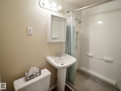 Full bathroom featuring a pedestal sink, white toilet, and a shower with built-in shelving - 79 Grosvenor Boulevard, St. Albert, AB 