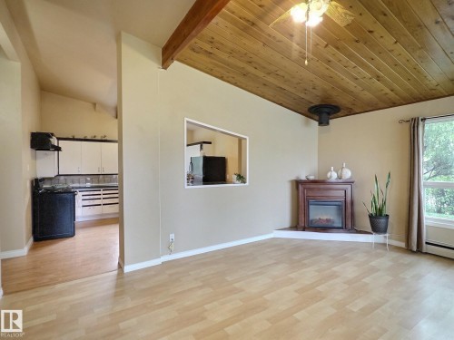 Living area featuring wood-finish flooring, a corner fireplace with a wood mantle, and a wood plank ceiling with exposed beam - 79 Grosvenor Boulevard, St. Albert, AB 