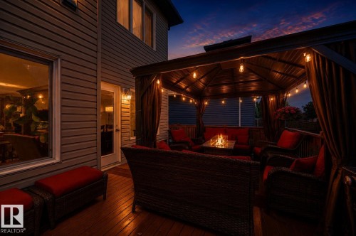 Expansive wood-finish deck featuring a covered gazebo with string lighting, a gas fire pit, and durable siding exterior - 101 Hilldowns Drive, Spruce Grove, AB 