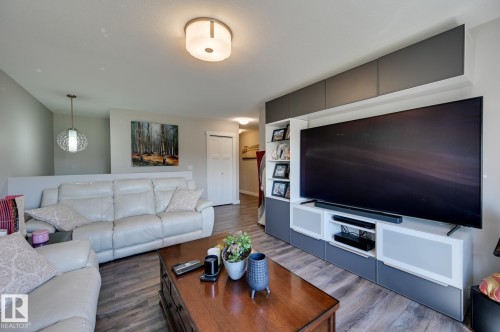 Open-concept living area featuring wood-finish flooring, a contemporary ceiling light fixture, a built-in media console with integrated shelving, and a decorative pendant light - 101 Hilldowns Drive, Spruce Grove, AB 
