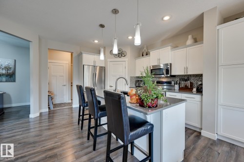 Kitchen featuring an island with seating, pendant lighting, stainless steel appliances, white cabinetry, and wood-finish flooring - 101 Hilldowns Drive, Spruce Grove, AB 