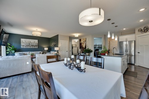 Open-concept living area featuring wood-finish flooring, a contemporary dining chandelier, and a kitchen island with pendant lighting - 101 Hilldowns Drive, Spruce Grove, AB 