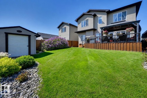 Spacious backyard featuring a substantial lawn, a large raised deck with a black gazebo, a detached storage shed, and mature landscaping with a flowering shrub - 101 Hilldowns Drive, Spruce Grove, AB 