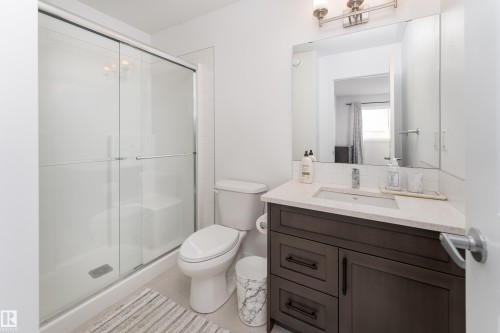 Full bathroom featuring a dark wood-finish vanity with an integrated sink and light-toned countertop, a frameless mirror, and a glass-enclosed shower with a sliding door - 2522 152 Avenue Nw, Edmonton, AB - Indoor Photo Showing Bathroom
