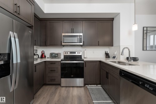 Kitchen featuring wood-finish cabinetry, stainless steel appliances, a white subway tile backsplash, light-toned countertops, and wood-finish laminate flooring - 2522 152 Avenue Nw, Edmonton, AB - Indoor Photo Showing Kitchen With Double Sink