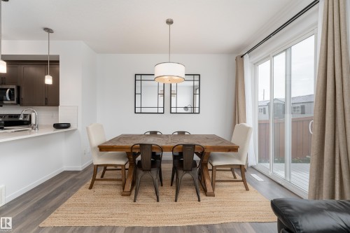 Open-concept dining area featuring wood-finish laminate flooring, a contemporary drum pendant light, and sliding glass doors - 2522 152 Avenue Nw, Edmonton, AB - Indoor Photo Showing Dining Room