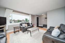 Living area featuring a large picture window, light-toned walls, and wood-finish flooring - 