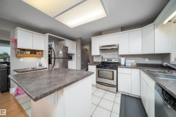 Kitchen featuring white cabinetry, dark countertops, stainless steel appliances, a center island, and tiled flooring - 