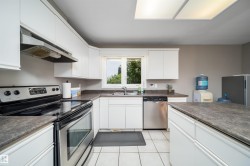 Bright kitchen featuring white cabinetry, a stainless steel range, a stainless steel dishwasher, a window over the sink, and a tiled floor - 