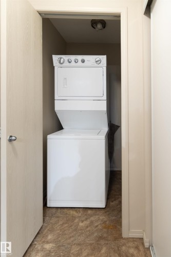 Dedicated laundry closet featuring a white stacked washer and dryer unit - #214 1188 Hyndman Rd Nw, Edmonton, AB - Indoor Photo Showing Laundry Room