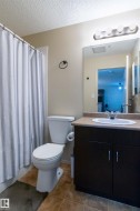 Bathroom featuring a dark wood-finish vanity with a single basin sink, light-toned countertop, and a contemporary four-bulb vanity light fixture - 