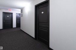 Corridor featuring dark paneled entry doors, textured white walls, recessed ceiling lighting, and dark carpet flooring - 