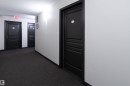 Corridor featuring dark paneled entry doors, textured white walls, recessed ceiling lighting, and dark carpet flooring - #214 1188 Hyndman Rd Nw, Edmonton, AB  - Indoor Photo Showing Other Room 