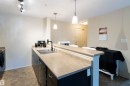 Contemporary kitchen featuring dark cabinetry, light countertops, and a double basin stainless steel sink with a matte black faucet - #214 1188 Hyndman Rd Nw, Edmonton, AB  - Indoor Photo Showing Kitchen With Double Sink 