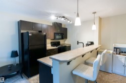 Kitchen featuring a breakfast bar with two pendant lights, dark wood-finish cabinetry, black appliances including a refrigerator and range, and track lighting - 