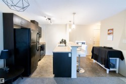 Modern kitchen featuring dark cabinetry, black appliances, light-toned countertops, and a breakfast bar with pendant lighting - 