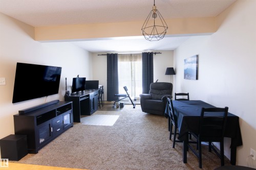 Expansive main living area featuring neutral-toned carpeting, light-colored walls, and a modern geometric pendant light fixture - #214 1188 Hyndman Rd Nw, Edmonton, AB - Indoor