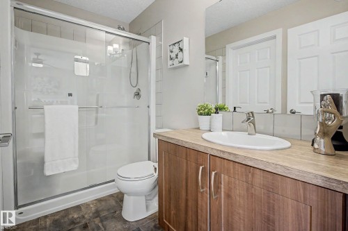 Bathroom featuring a glass-enclosed shower, white toilet, single vanity with wood-finish cabinetry, a vessel sink, and a large mirror - 22609 94A Avenue Nw, Edmonton, AB - Indoor Photo Showing Bathroom