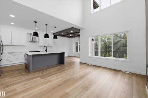 Open-concept living space featuring high ceilings, contemporary kitchen with a large island, wood-finish flooring, and expansive windows - 915 Elderberry Landing Nw, Edmonton, AB - Indoor Photo Showing Kitchen