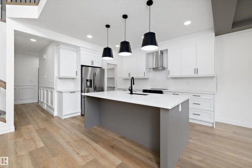 Contemporary kitchen featuring a large central island with a solid surface countertop, overhead pendant lighting, and light wood-finish flooring - 915 Elderberry Landing Nw, Edmonton, AB - Indoor Photo Showing Kitchen With Upgraded Kitchen