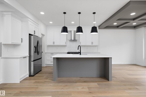 Modern kitchen featuring a central island with a waterfall countertop, sleek black pendant lighting, stainless steel appliances, white shaker cabinetry, and wood-finish flooring - 915 Elderberry Landing Nw, Edmonton, AB - Indoor Photo Showing Kitchen With Upgraded Kitchen