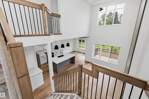Two-story living area with hardwood-finish flooring, a contemporary kitchen island with a dark sink, and multiple large windows - 915 Elderberry Landing Nw, Edmonton, AB - Indoor Photo Showing Other Room