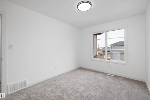 Bright room featuring a large window, neutral gray carpeting, white walls, and a contemporary flush-mount ceiling light fixture - 915 Elderberry Landing Nw, Edmonton, AB - Indoor Photo Showing Other Room