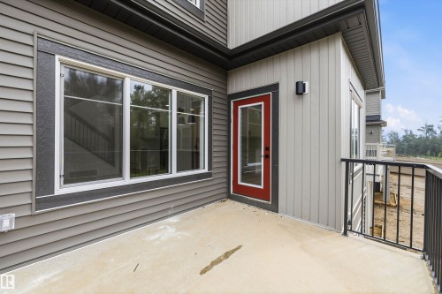 Spacious private balcony with concrete flooring and black metal railing, featuring a red entry door with glass paneling, a contemporary exterior light fixture, and large multi-pane windows - 915 Elderberry Landing Nw, Edmonton, AB - Outdoor With Exterior