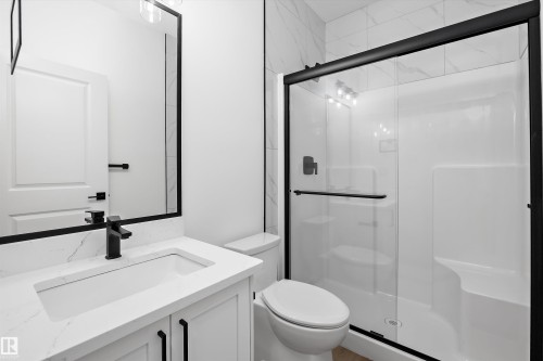 Bathroom featuring a walk-in shower with clear glass enclosure and black trim, a white vanity with integrated sink and quartz-finish countertop, a black-framed mirror, and matte black fixtures - 915 Elderberry Landing Nw, Edmonton, AB - Indoor Photo Showing Bathroom