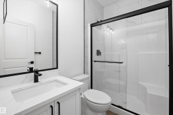 Bathroom featuring a walk-in shower with clear glass enclosure and black trim, a white vanity with integrated sink and quartz-finish countertop, a black-framed mirror, and matte black fixtures - 
