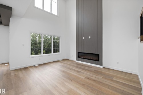 Vaulted ceilings with upper windows, a linear electric fireplace with a dark vertical shiplap accent wall, and wood-finish flooring - 915 Elderberry Landing Nw, Edmonton, AB - Indoor Photo Showing Living Room With Fireplace