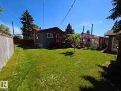 Expansive backyard featuring a lush lawn, a multi-paneled greenhouse, a raised wood deck with stairs, mature perimeter trees, and a privacy fence - 