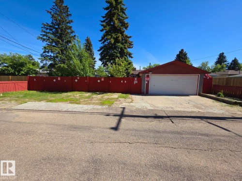 Detached garage with a single white door, red siding, and a red roof, positioned behind a gravel driveway - 10404 116 Avenue, Edmonton, AB 