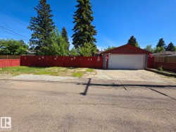 Detached garage with a single white door, red siding, and a red roof, positioned behind a gravel driveway - 