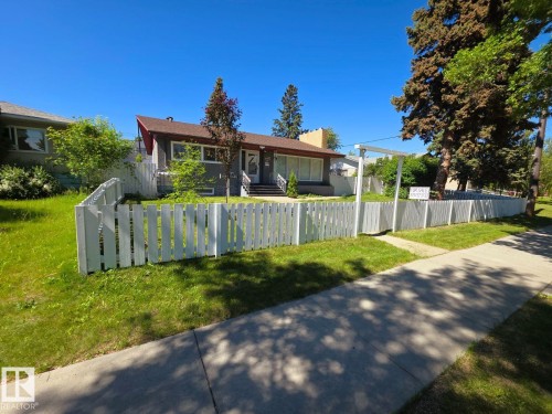 Gray exterior home with a partial white picket fence, mature trees, and a concrete sidewalk - 10404 116 Avenue, Edmonton, AB 