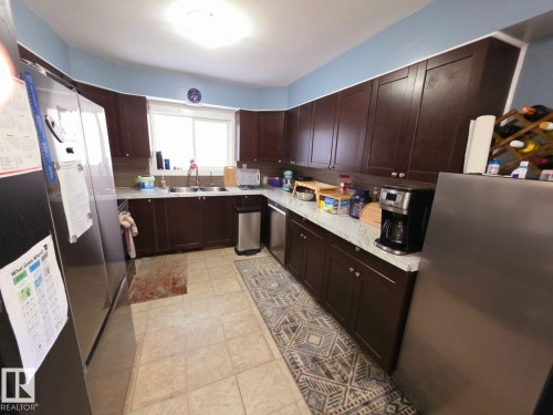Kitchen featuring dark wood-finish cabinetry, light-toned tiled flooring, and a stainless steel French door refrigerator - 10404 116 Avenue, Edmonton, AB 