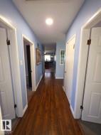 Hallway featuring wood-finish flooring, light blue wall paint, white trim, and recessed lighting - 