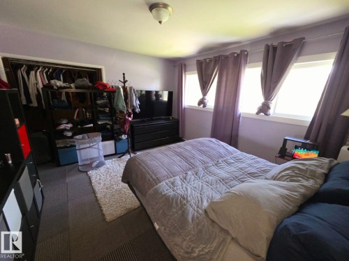 Bedroom featuring a wall of three windows, a built-in closet with shelving, a ceiling-mounted light fixture, and tile flooring - 10404 116 Avenue, Edmonton, AB 
