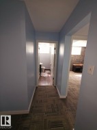 Hallway with patterned carpet flooring, light blue walls, and white baseboards - 