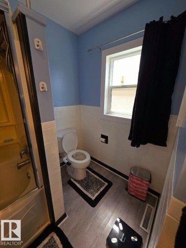 Bathroom featuring a combination tub/shower, toilet, and a window with white trim - 10404 116 Avenue, Edmonton, AB 