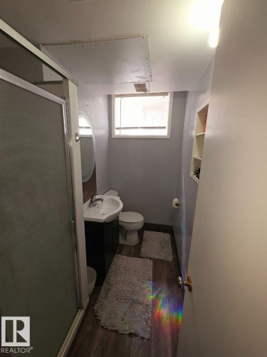 Bathroom featuring a glass-enclosed shower, a vanity with a white basin sink, wood-finish flooring, and a window with horizontal blinds - 10404 116 Avenue, Edmonton, AB 