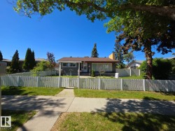 Front exterior featuring a white picket fence, mature trees, a concrete walkway, a covered entry porch, and a shingle roof - 