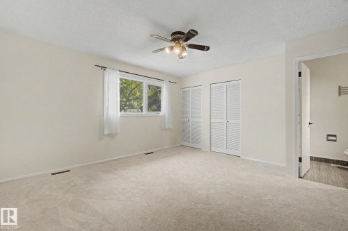 Spacious room featuring neutral carpeting, a large window, two bi-fold louvered closets, a ceiling fan with integrated lighting, and direct access to a separate area with dark-toned floor tiling - 170 Westridge Rd, Edmonton, AB - Indoor Photo Showing Other Room