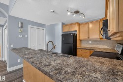Kitchen featuring an extended peninsula with a double basin sink, light wood cabinetry, stone-look countertops, and a tiled backsplash - 