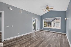 Vaulted ceiling room featuring wood-finish flooring, a ceiling fan, and large windows - 