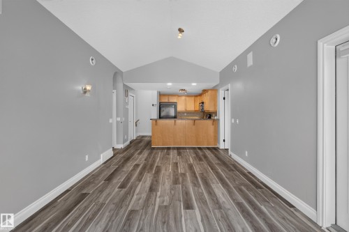 Open-concept living area featuring wood-finish flooring, vaulted ceilings, and a kitchen with light wood cabinetry and built-in appliances - 18 2565 Hanna Crescent, Edmonton, AB 