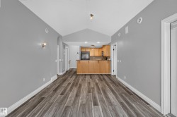 Open-concept living area featuring wood-finish flooring, vaulted ceilings, and a kitchen with light wood cabinetry and built-in appliances - 