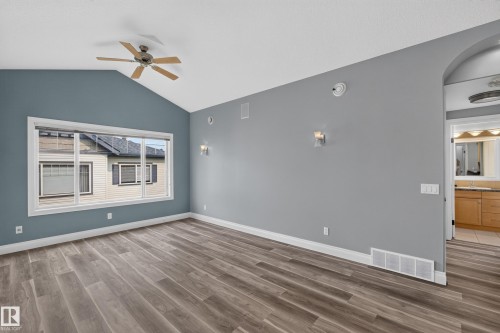Spacious room featuring vaulted ceilings, a large multi-pane window, wood-finish flooring, a ceiling fan, and wall-mounted sconces - 18 2565 Hanna Crescent, Edmonton, AB 