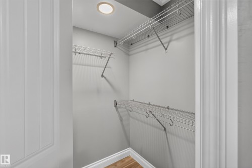 Recessed ceiling light illuminating a walk-in closet featuring multiple levels of wire shelving, integrated hanging rods, and wood-finish flooring with white baseboards - 18 2565 Hanna Crescent, Edmonton, AB 